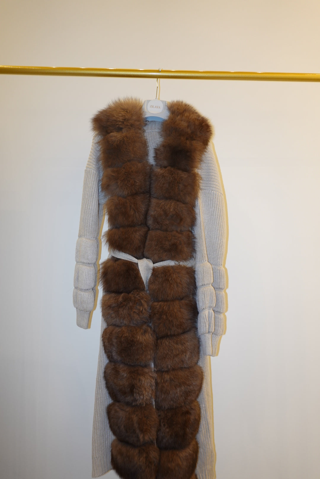Brown fur-trimmed jackets/cardigan on a rack against a white wall.