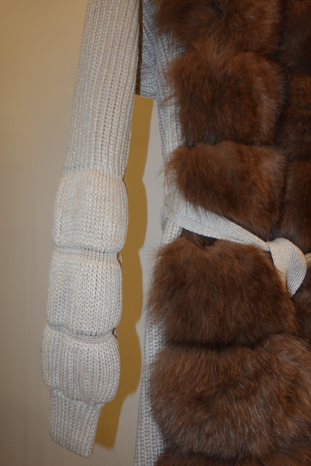 Brown fur-trimmed jackets/cardigan on a rack against a white wall.